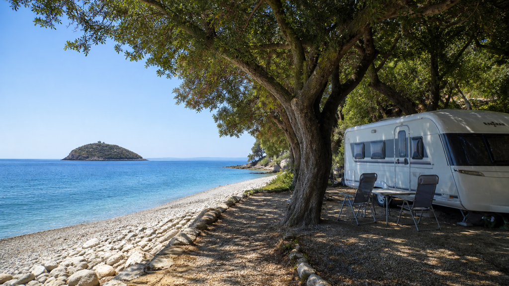 Camping sfeerfoto van een caravanplaats aan een kiezelstrand tegenover Gallinara